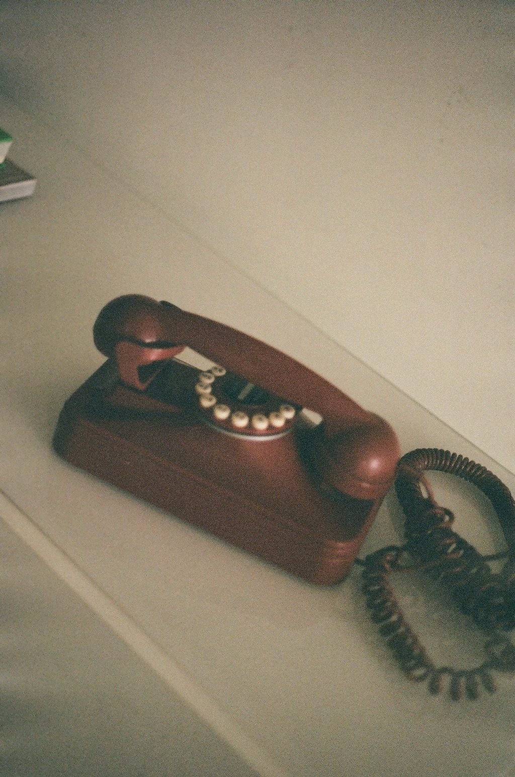 A vintage oxblood rotary telephone resting on a white shelf in warm light